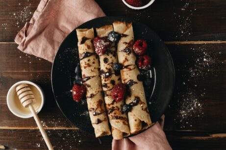 Rolované pohánkové palacinky s čokoládovou polevou, malinami a čučoriedkami na tmavom drevenom stole